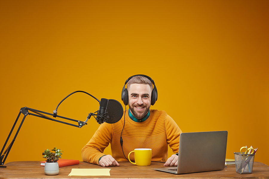 Horizontal studio portrait of young adult man working as radio presenter sitting at table in his workplace looking at camera
